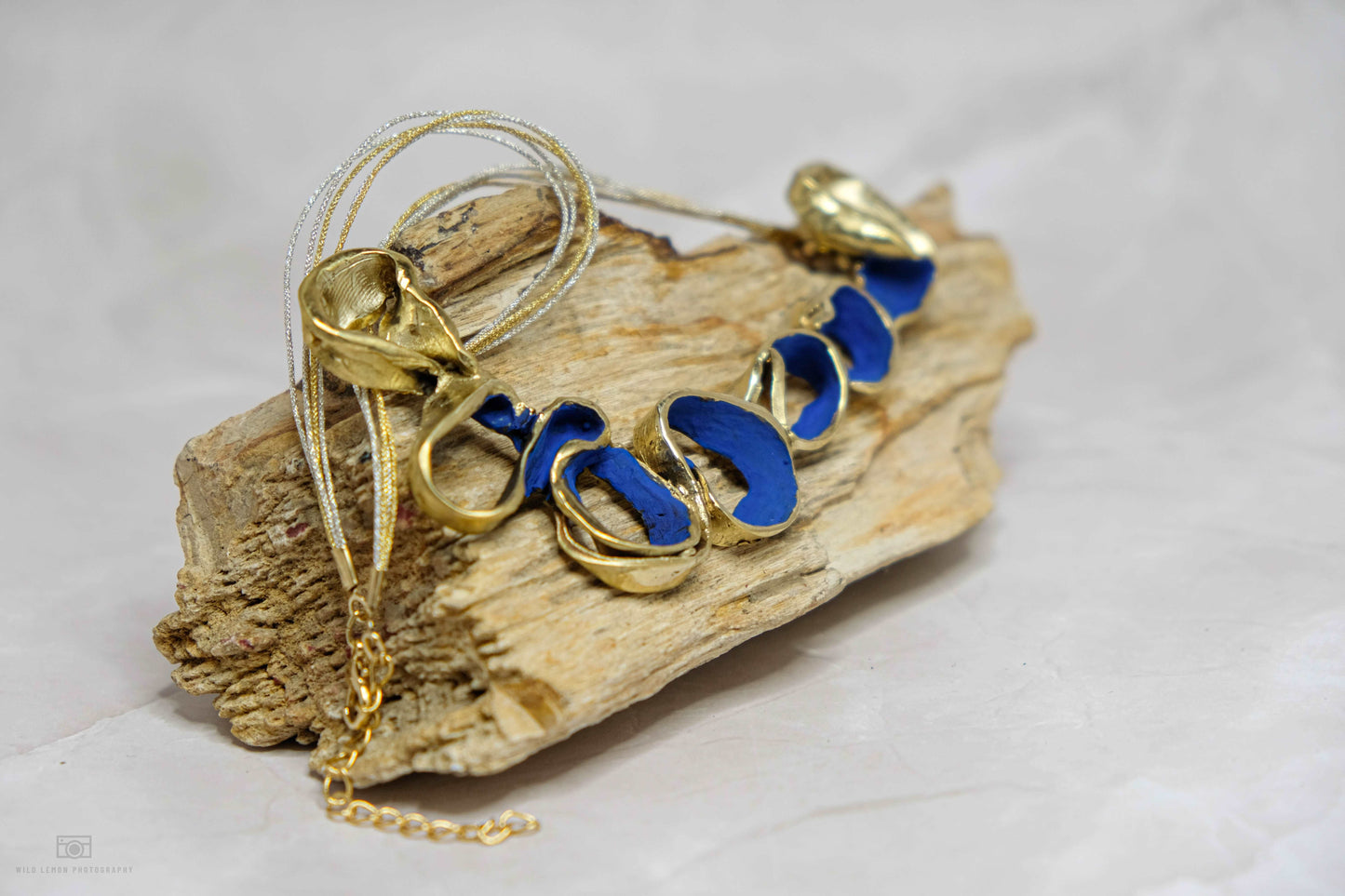Gold-tone necklace with blue oval link beads and shell charm on driftwood