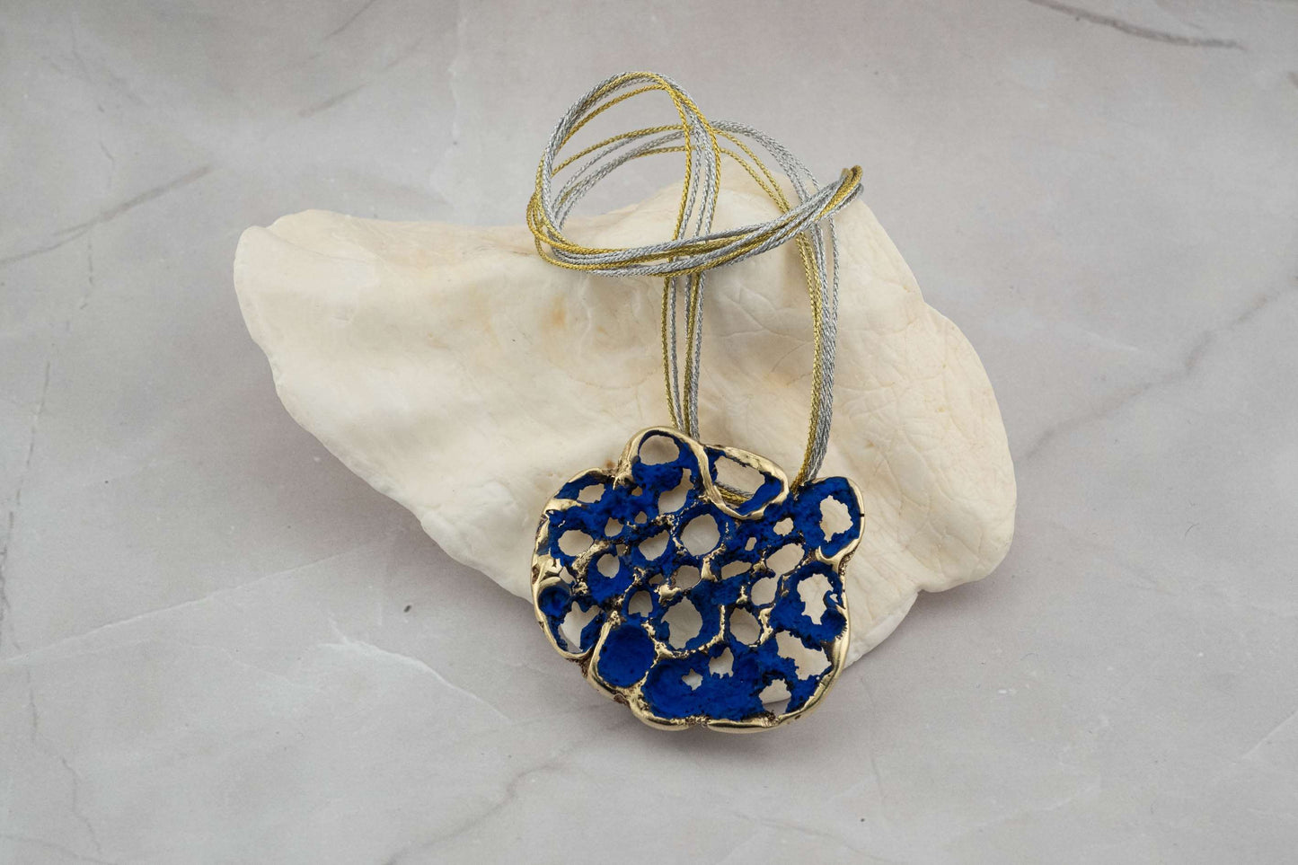 Perforata Lux pendant necklace, blue perforated oval pendant with multi-strand cord