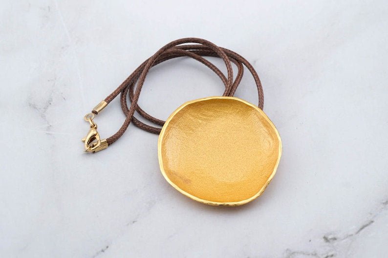 Gold-tone round pendant necklace with brown cord, shown from above