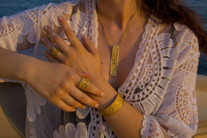 Gold hammered ring on finger, worn with other gold jewelry and lace sleeve