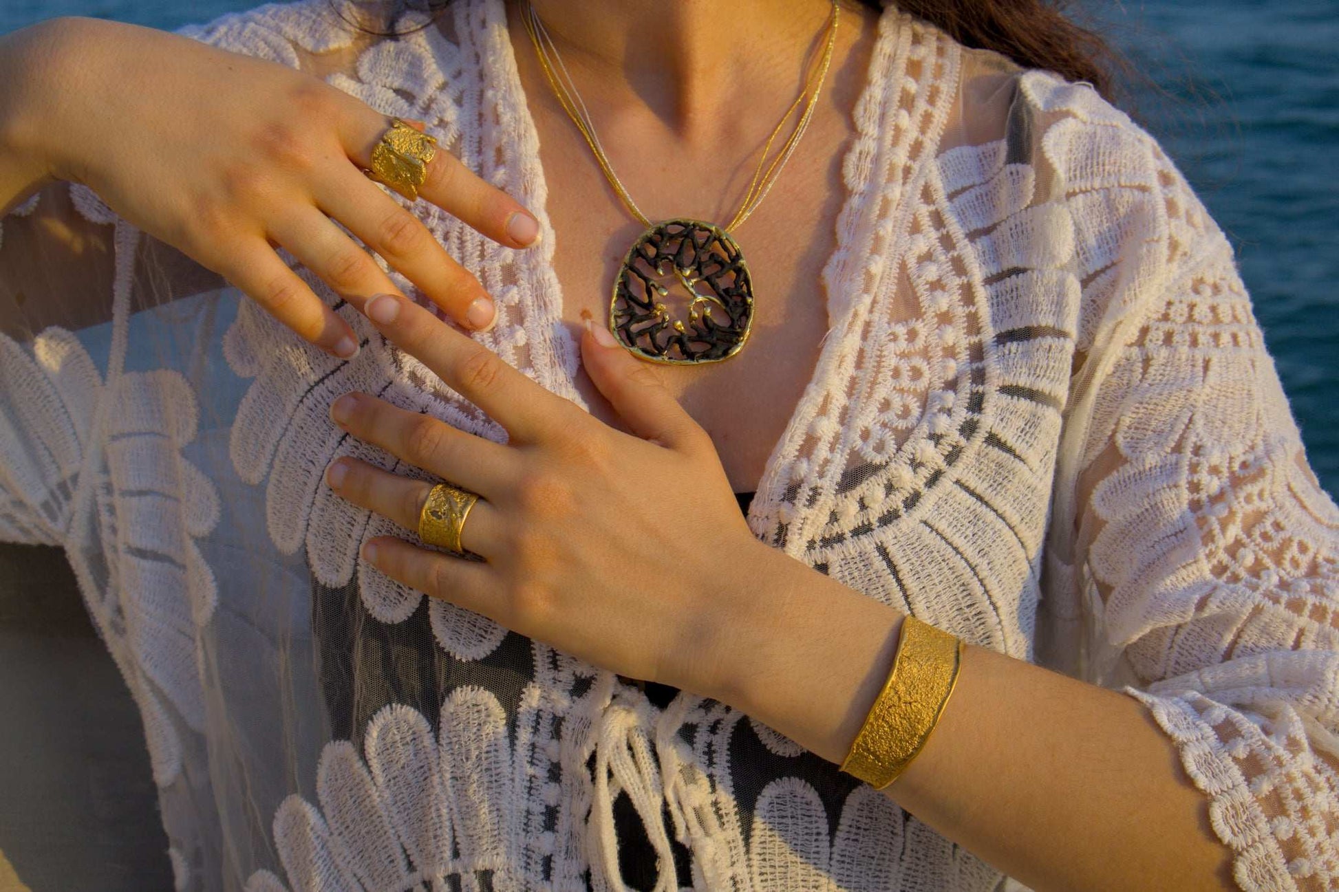 Gold textured ring on finger with matching bracelet cuff, worn with lace top