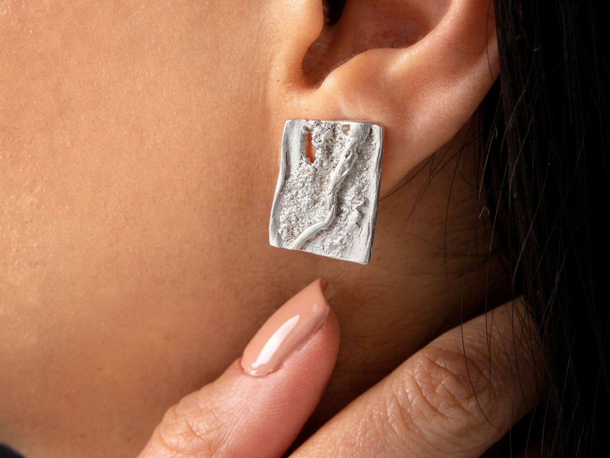 Silver square stud earrings on ear with textured layered face