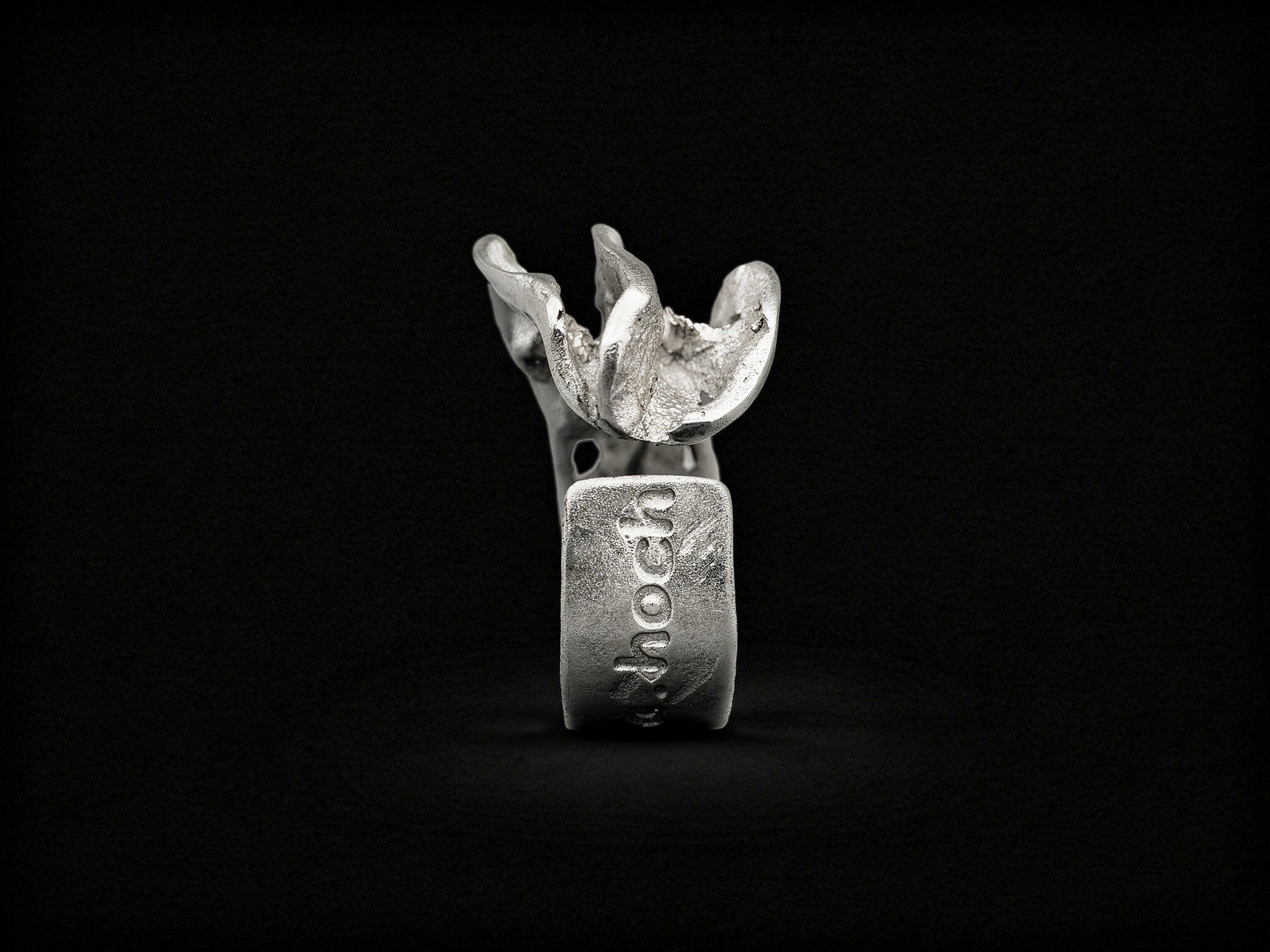 Silver sculpted ring, front view with raised jagged crest and stamp on band