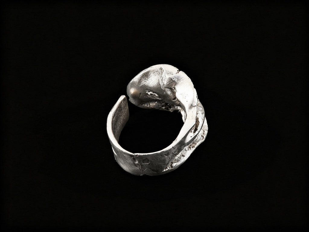 Silver sculpted ring side view with open, wave-like metalwork and raised top