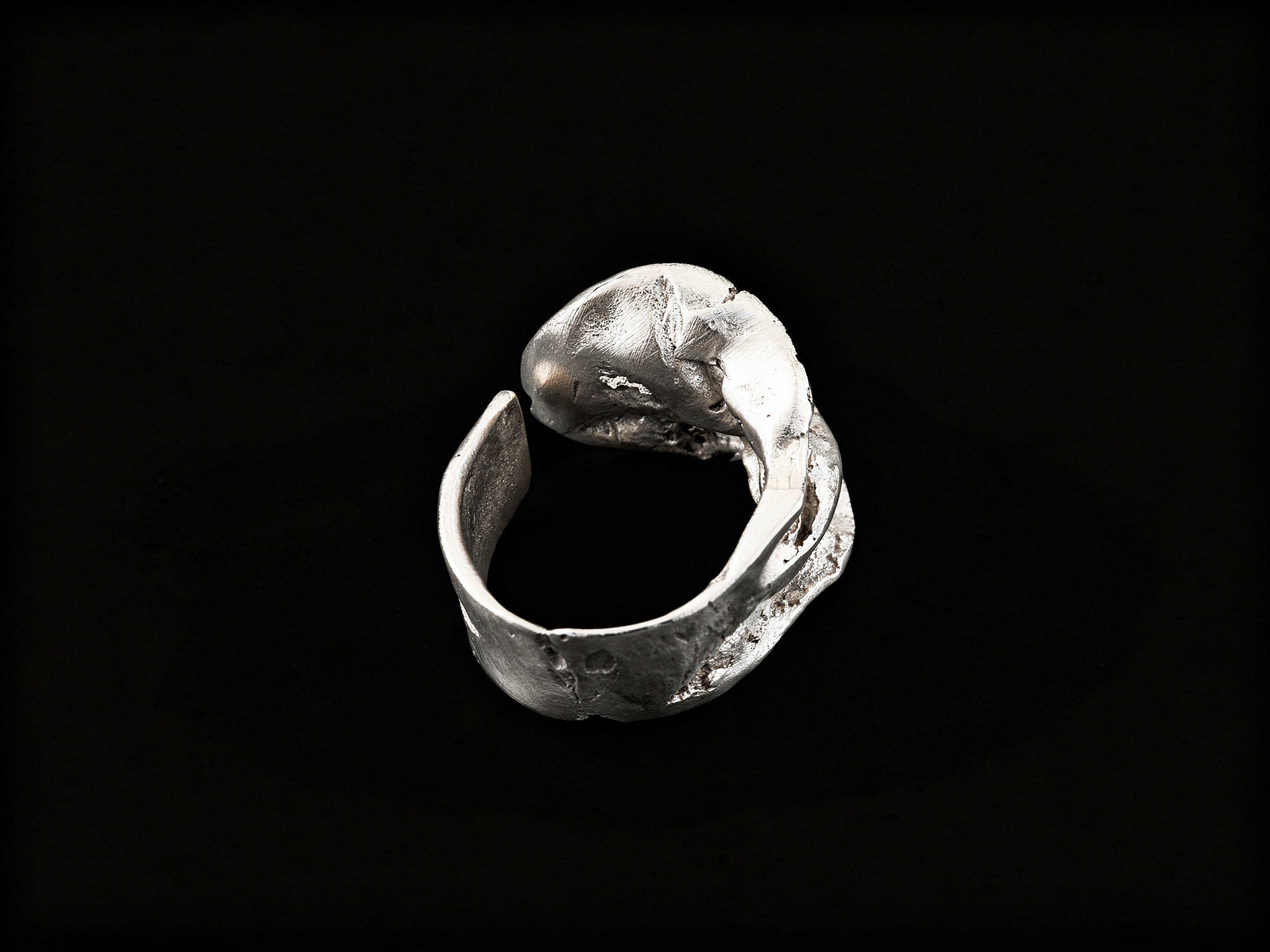 Silver sculpted ring side view with open, wave-like metalwork and raised top