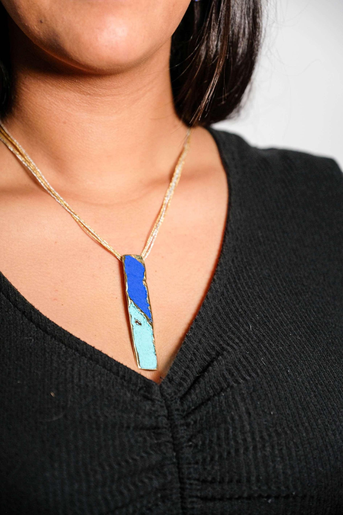 Gold-tone pendant necklace with blue and turquoise enamel teardrop pendant at neckline