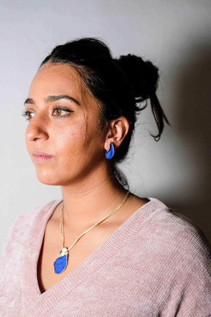 Gold-tone necklace with blue teardrop pendant, worn at neckline