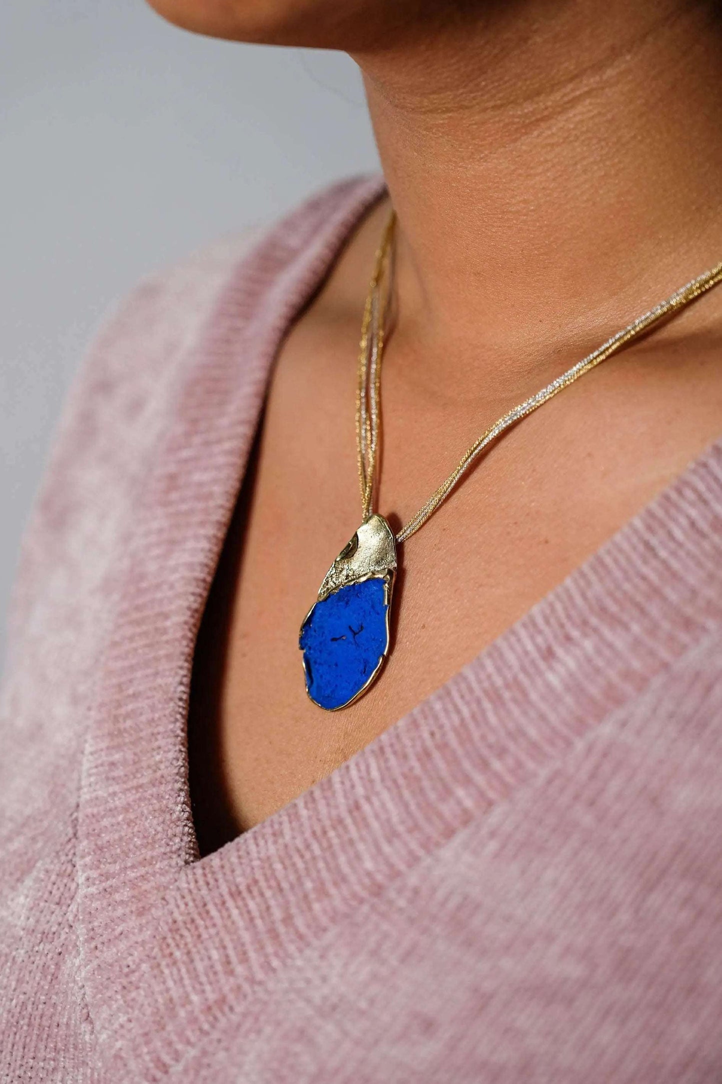 Gold-tone necklace with blue teardrop pendant, worn on model