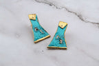 Turquoise statement earrings with gold-edged triangular cutouts, flat lay