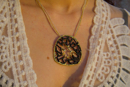 Orbis pendant close-up: dark round filigree with gold-toned branching pattern