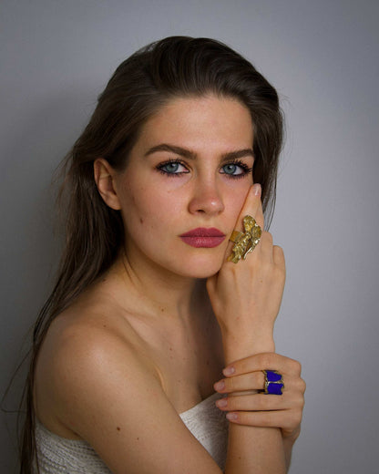 Gold-tone ring with pale green stone, plus a blue ring on fingers