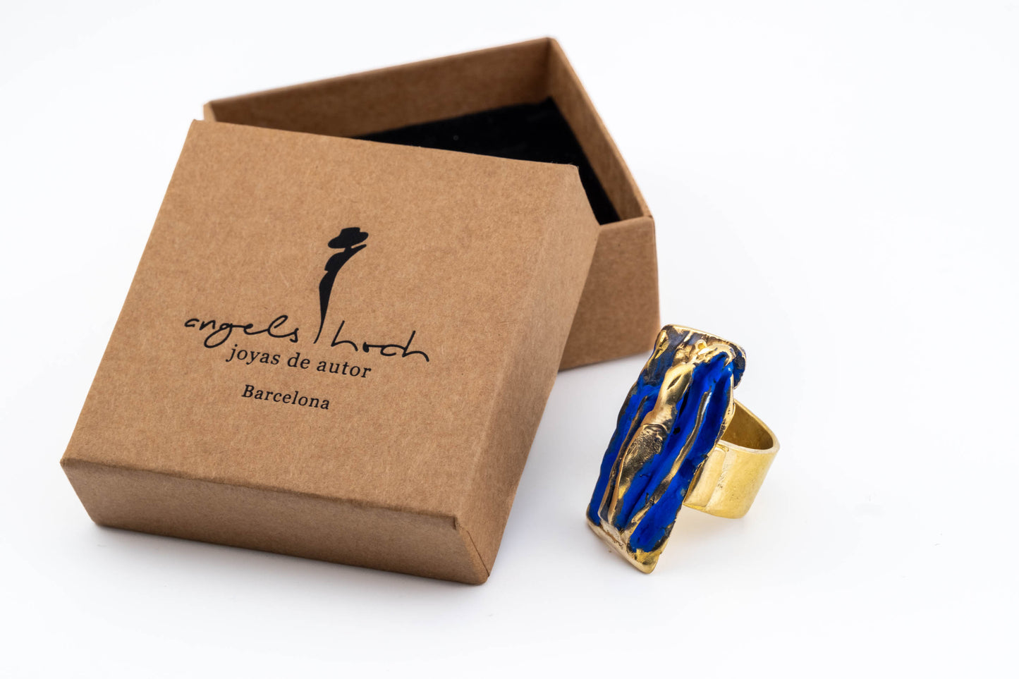 Blue and gold-tone rectangular sculpted ring beside a kraft gift box
