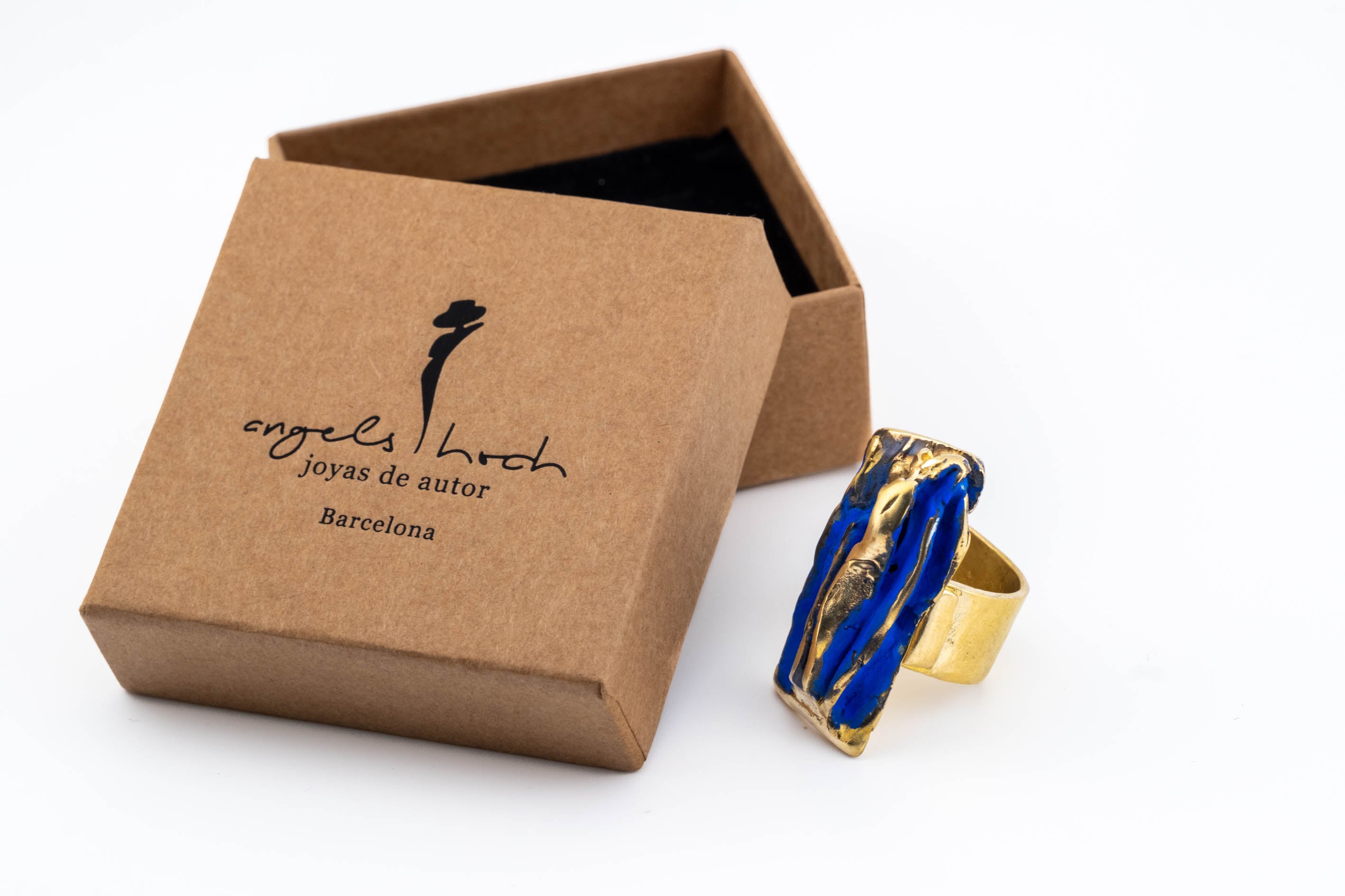 Blue and gold-tone rectangular sculpted ring beside a kraft gift box