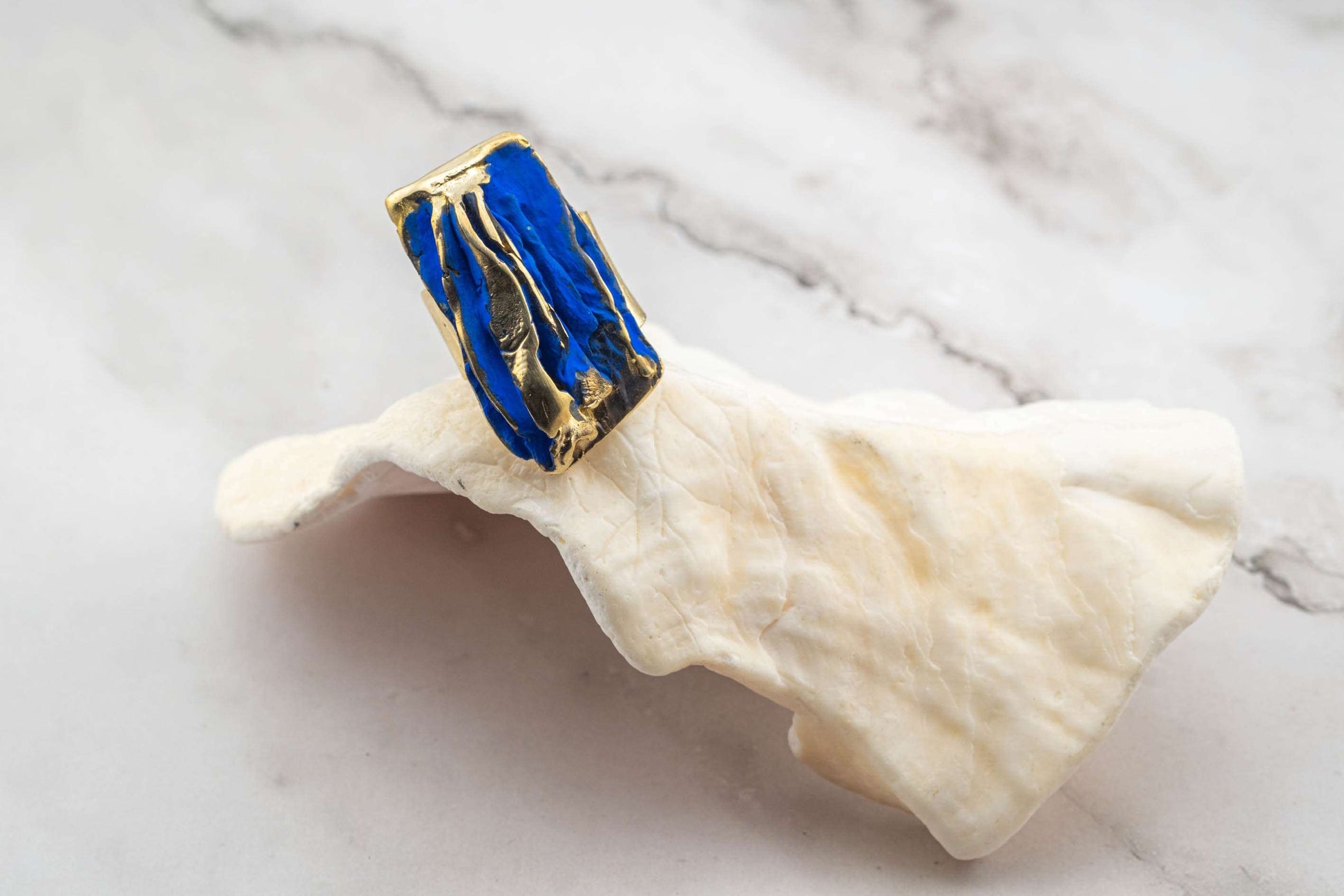 Rectangular blue resin and gold-tone sculpted ring on light cloth