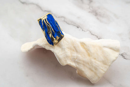 Rectangular blue resin and gold-tone sculpted ring on light cloth