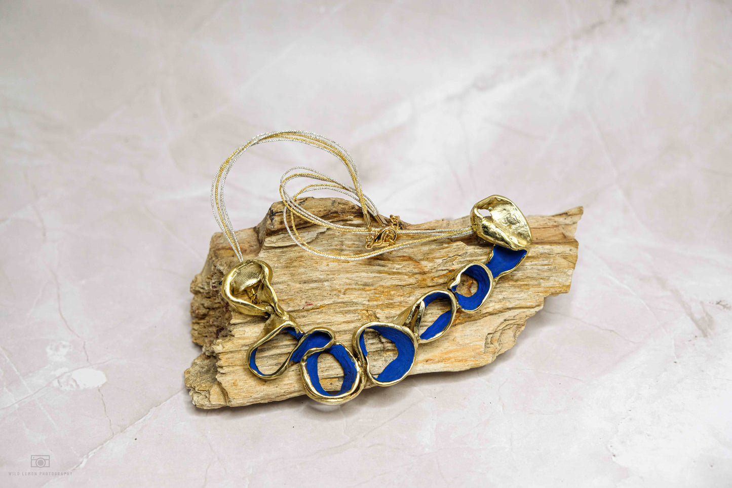 Gold-tone Ocean Harmony necklace with blue oval link beads on driftwood