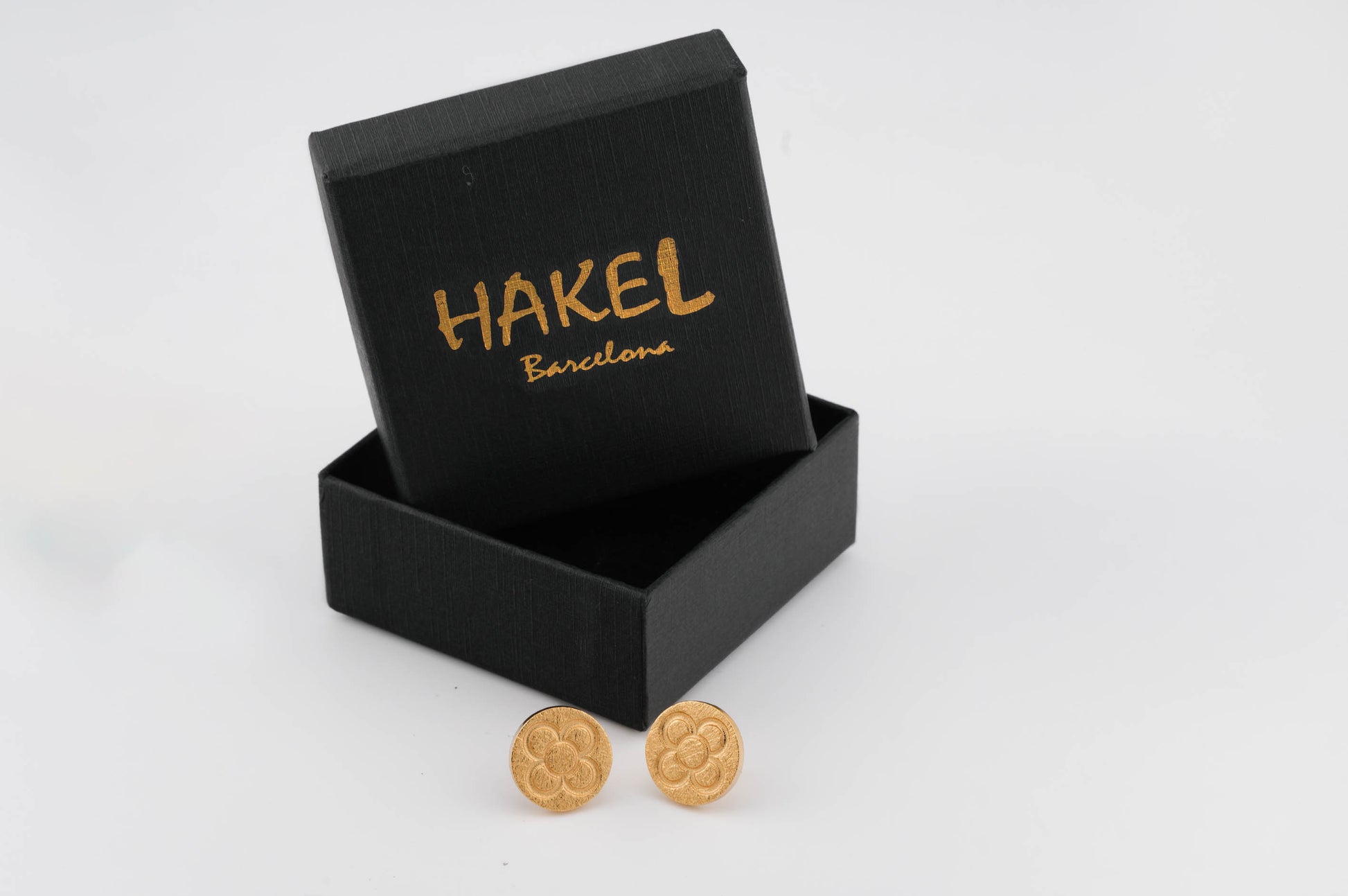 Gold round stud earrings with raised flower pattern beside an open gift box