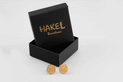 Gold round stud earrings with raised flower pattern beside an open gift box