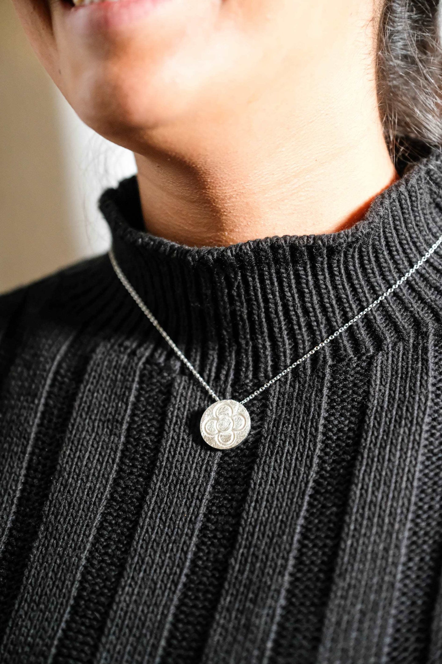 Silver round flower pendant necklace on chain, worn on dark ribbed knit