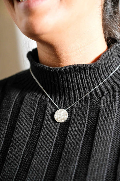 Silver round flower pendant necklace on chain, worn on dark ribbed knit