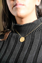 Collar con colgante redondo de flor de oro en cadena, usado en un suéter de punto acanalado oscuro