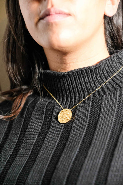 Gold round flower pendant necklace on chain, worn on dark ribbed knit