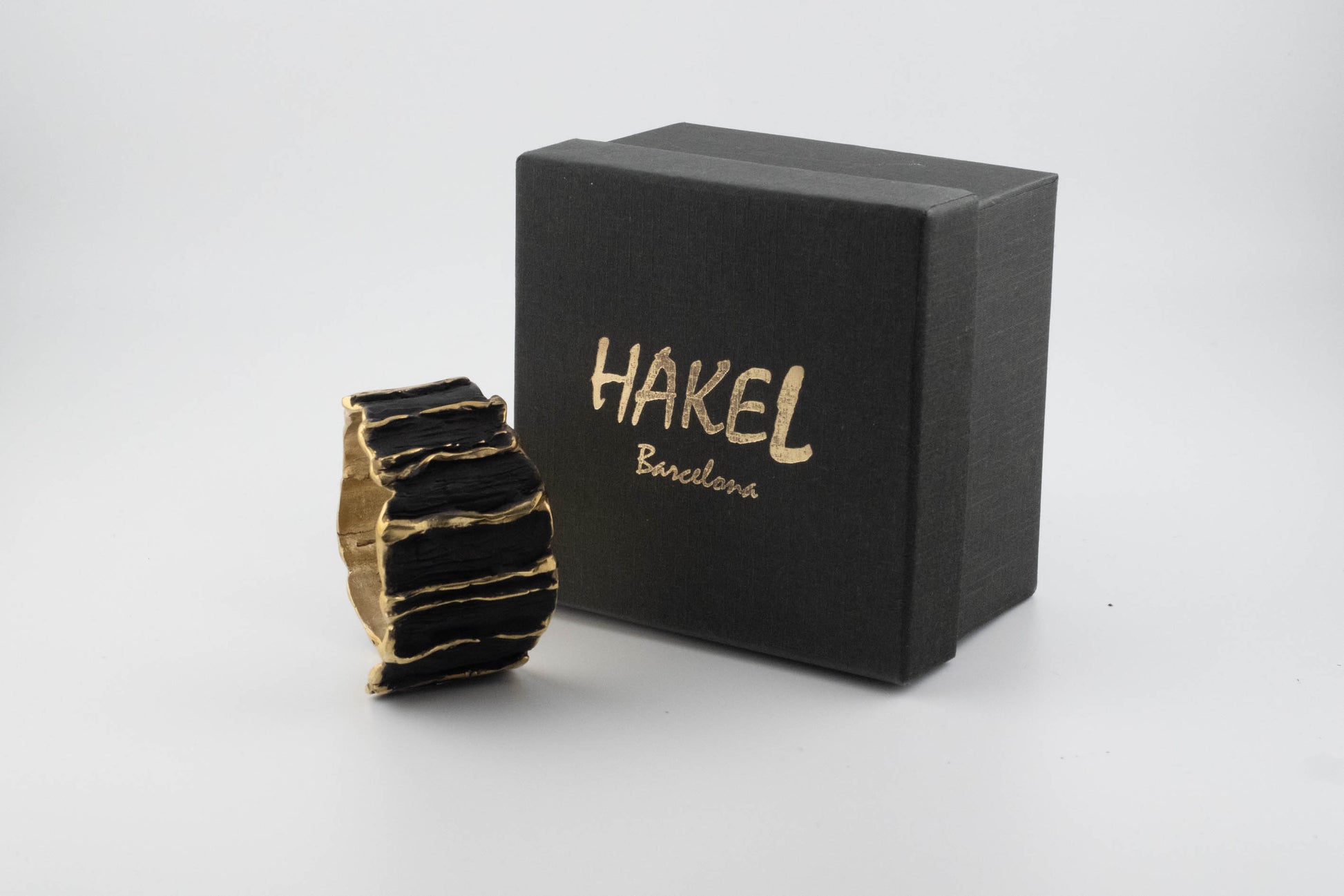 Gold-tone sculpted cuff bracelet next to HAKEL Barcelona gift box