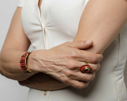 Red sculpted cuff bracelet with gold accents, worn on wrist with ring