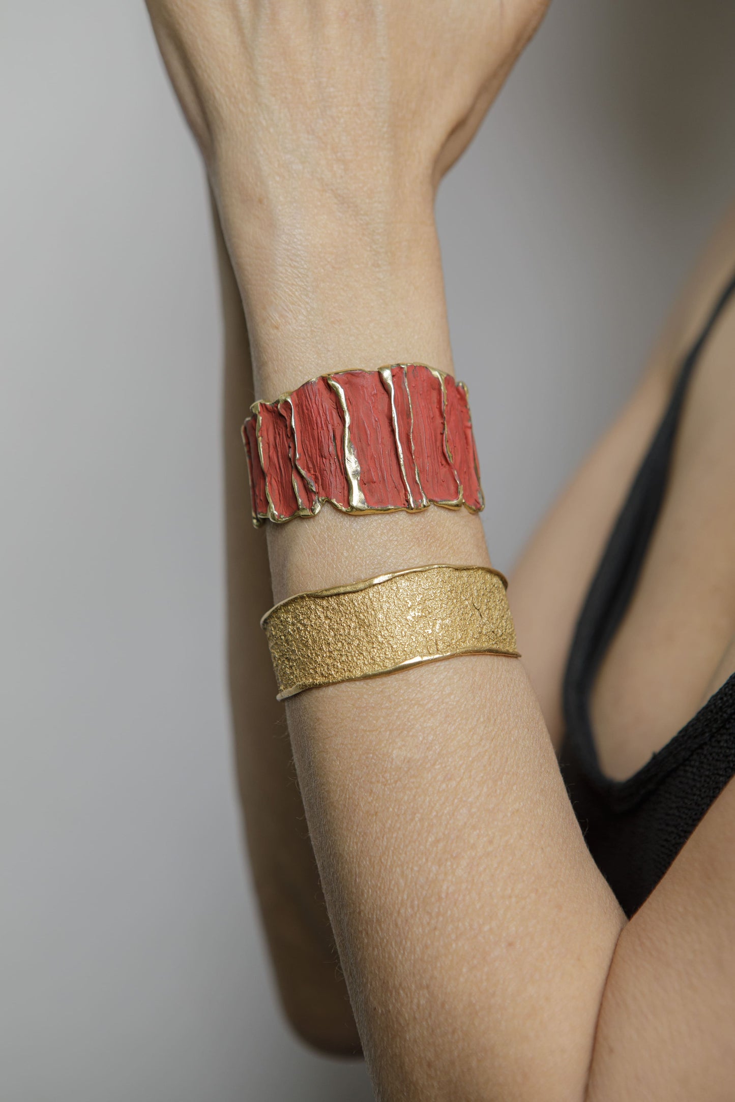 Red sculpted cuff bracelet with textured panels and gold band, worn on arm