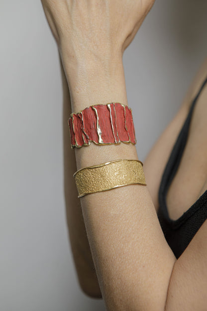 Red sculpted cuff bracelet with textured panels and gold band, worn on arm