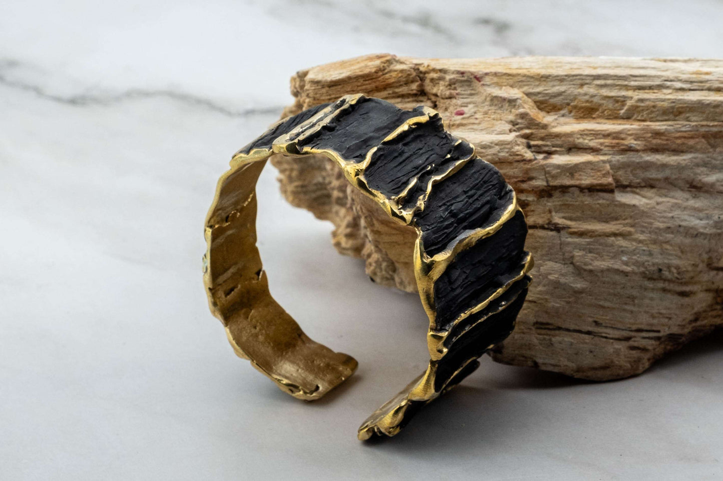 Black sculpted cuff bracelet with gold trim, textured ridges close-up