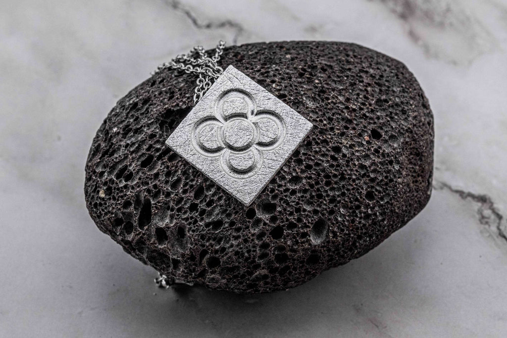 Penjoll de flor quadrada daurada sobre cadena sobre expositor de pedra fosca