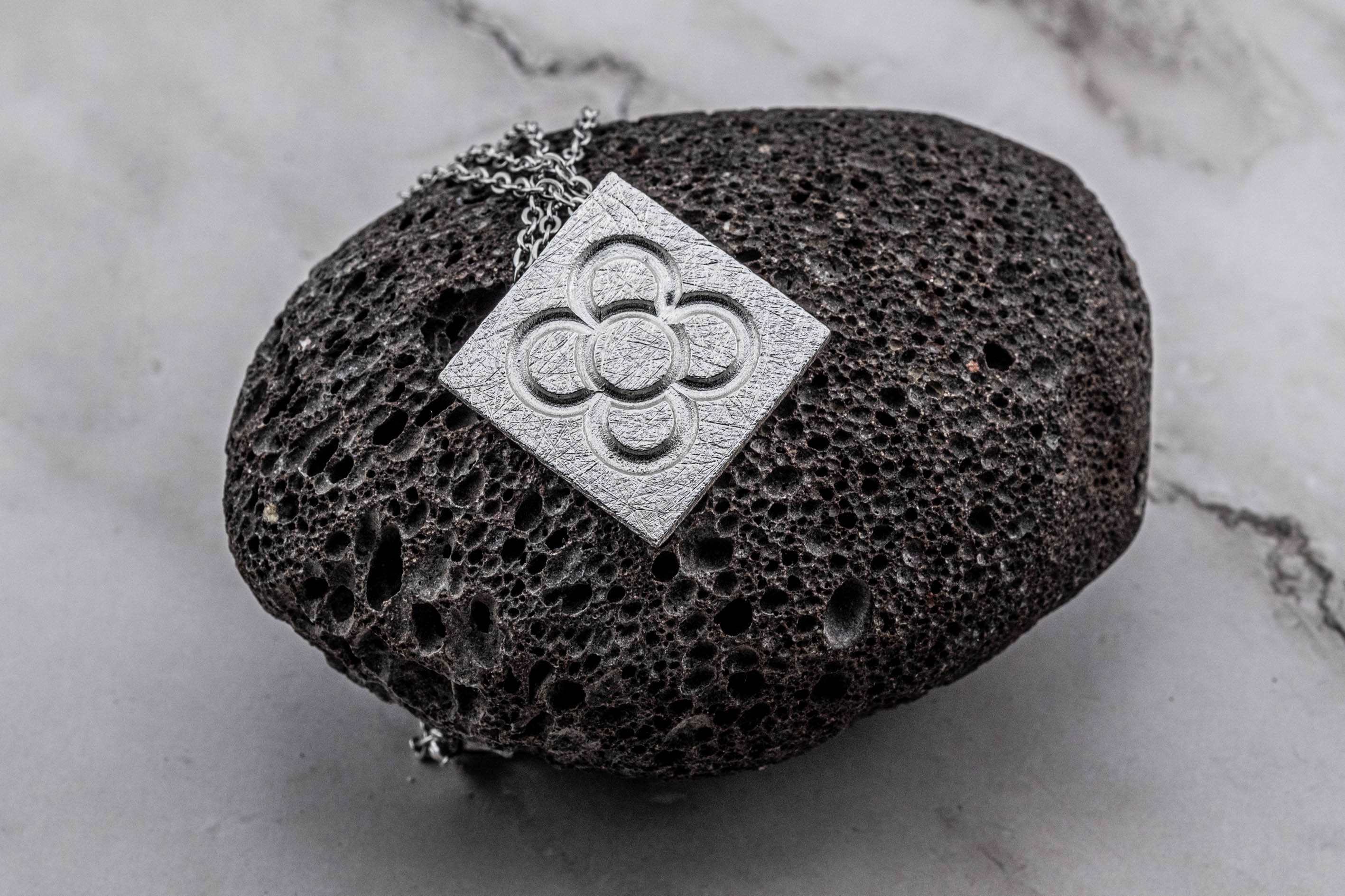 Penjoll de flor quadrada daurada sobre cadena sobre expositor de pedra fosca