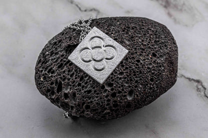Silver square flower pendant on chain over dark stone display