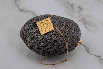 Gold square flower pendant on chain over dark stone display