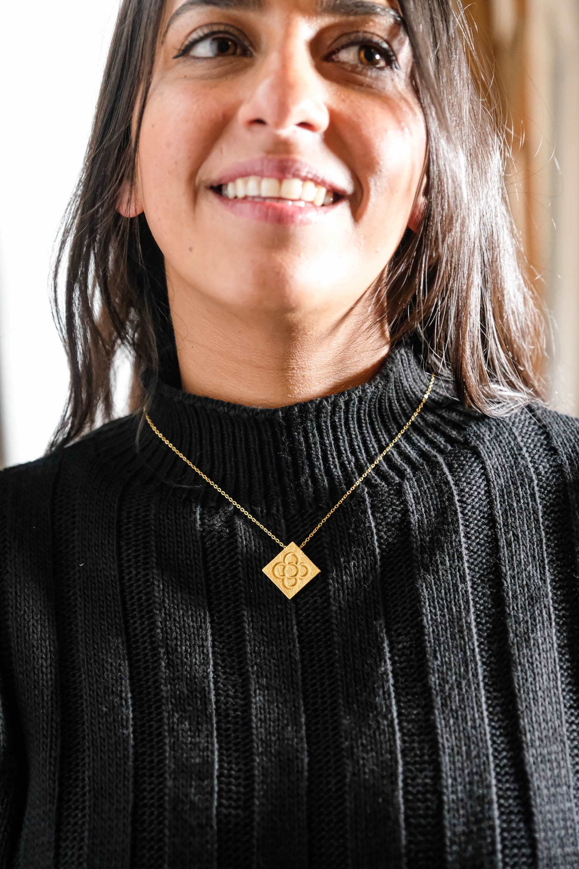 Gold square flower pendant necklace worn on a ribbed black sweater