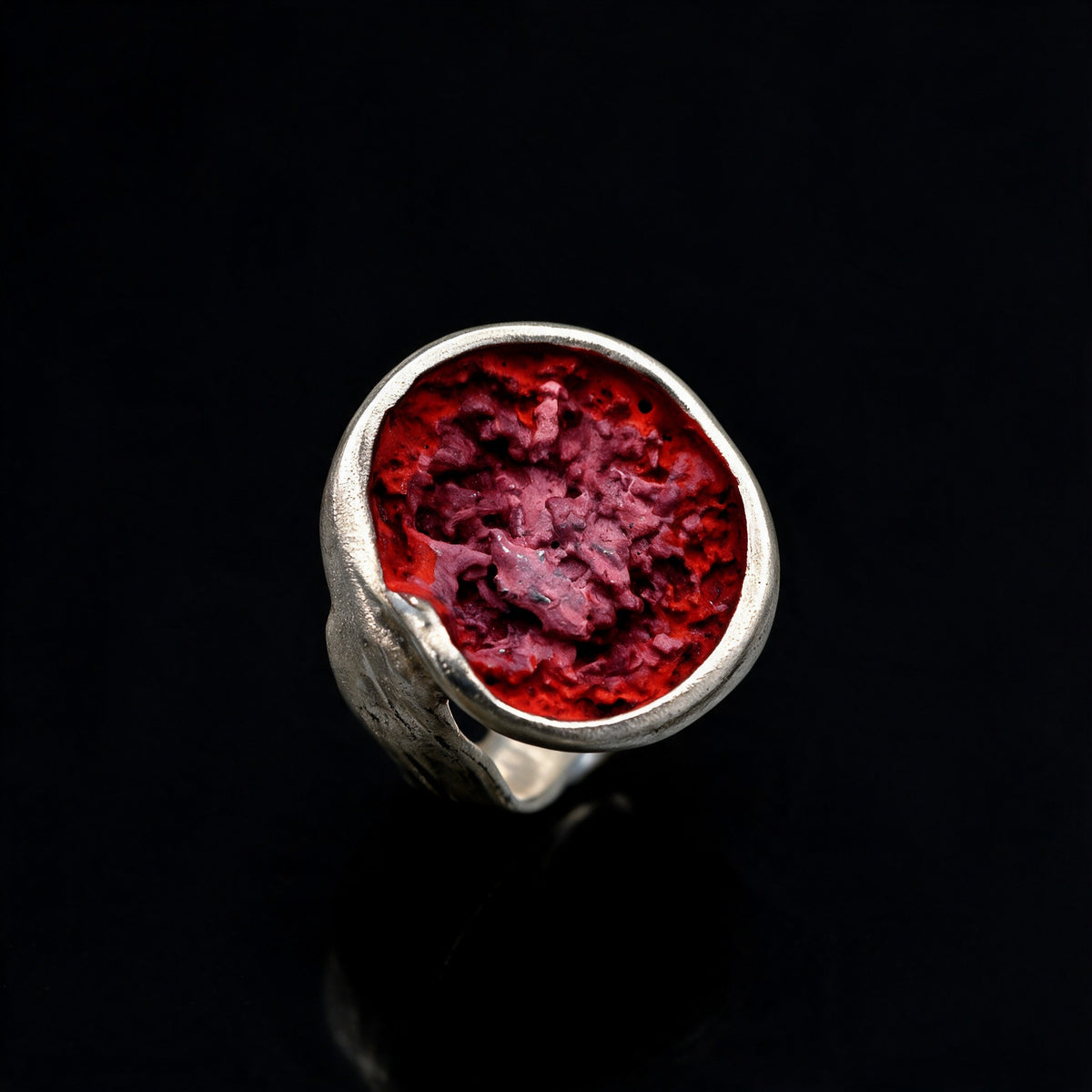 Silver ring with a raised oval bezel and textured red crater-like center