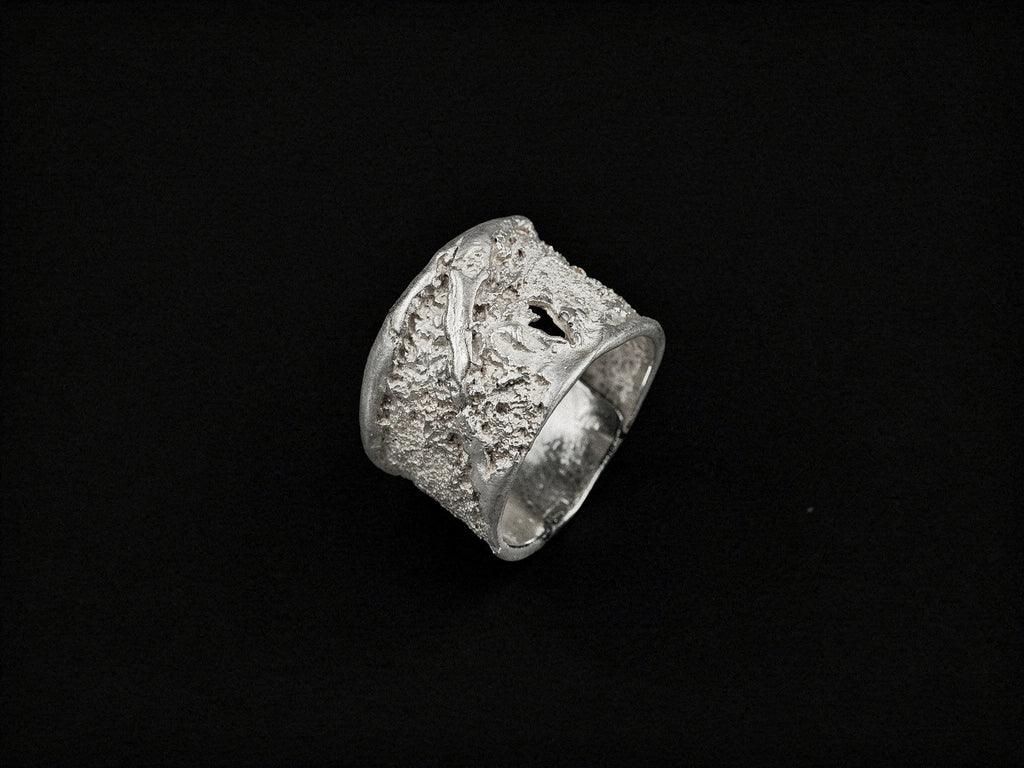 Anell de plata amb textura d'estrat amb incrustacions fosques, silueta quadrada gruixuda