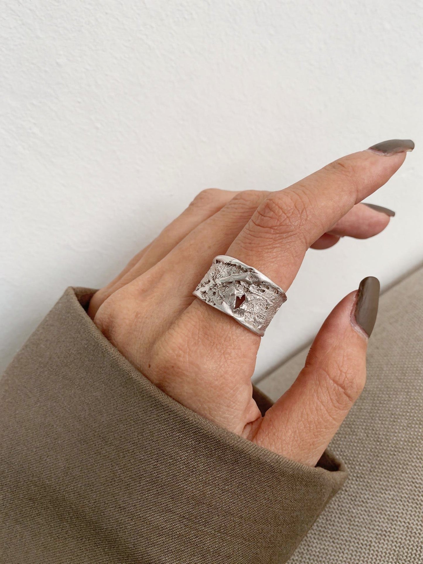 Silver strata ring on hand, rectangular textured top and wide open band