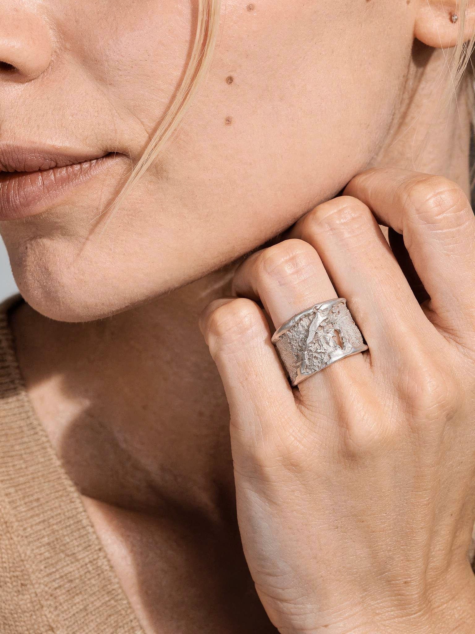 Silver strata ring on finger, square textured face with brushed silver finish