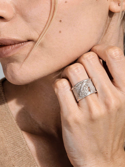 Silver strata ring on finger, square textured face with brushed silver finish