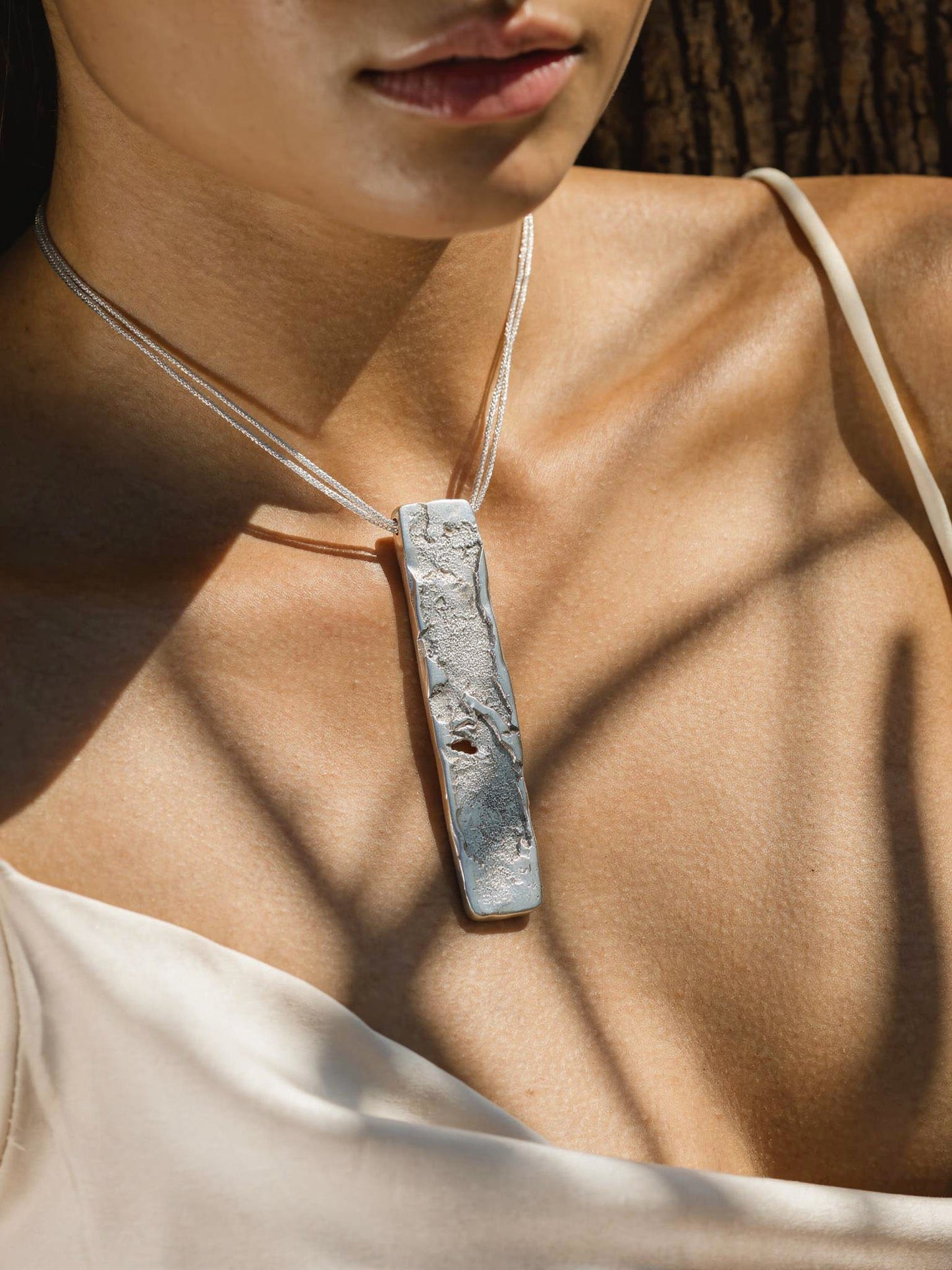 Silver strata necklace worn on neckline with rectangular hammered pendant