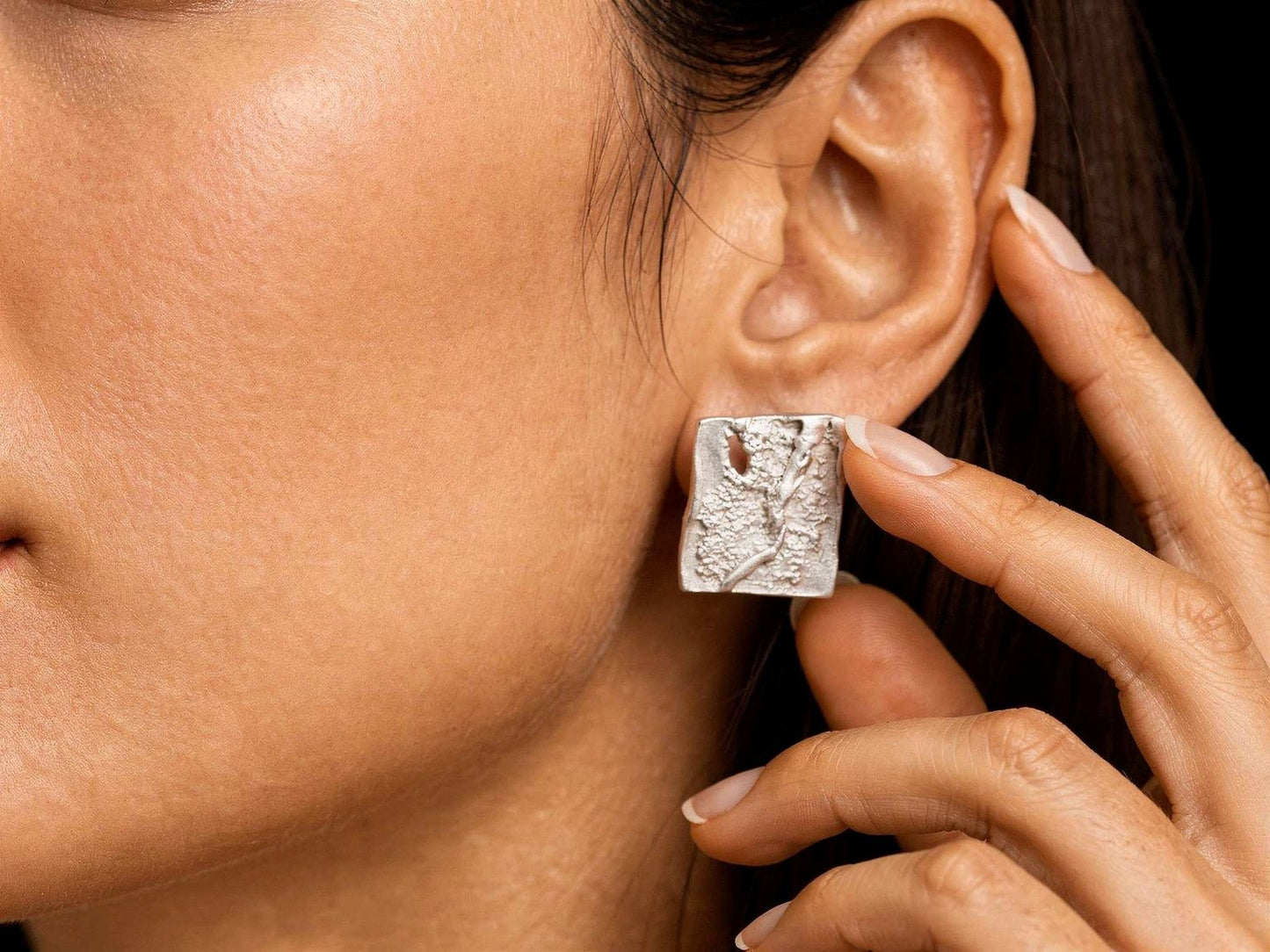 Silver square stud earrings on ear, close-up of textured square fronts