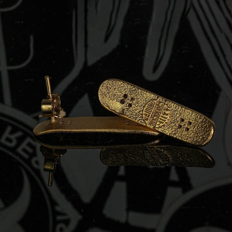 Skateboard stud earrings in gold tone, skateboard-shaped studs with perforation details.