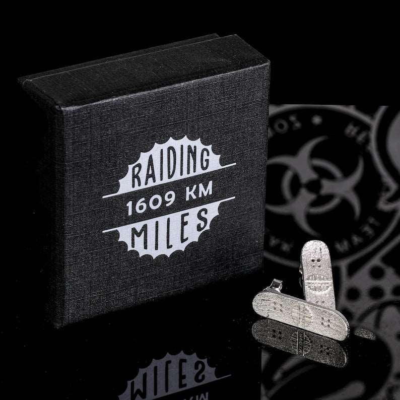 Silver skateboard stud earrings beside a dark gift box.