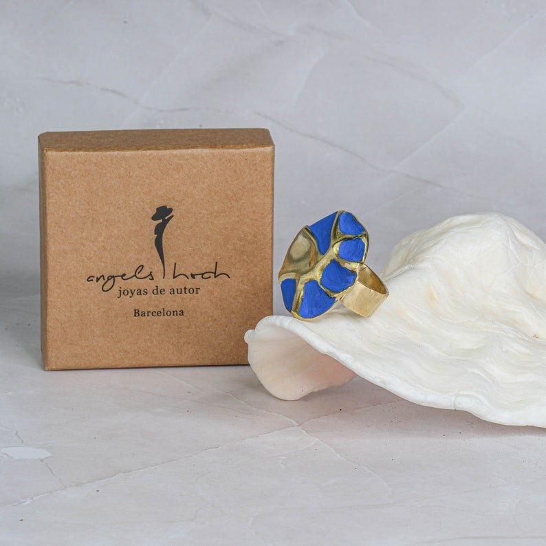 Blue enamel gold-tone concept ring on white marble surface
