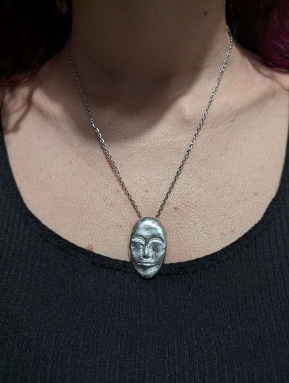 Silver face-mask pendant necklace on a collarbone with a fine chain link