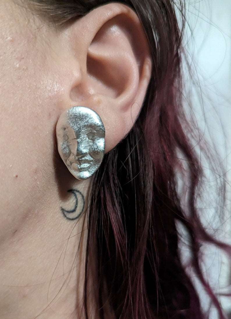 Silver oval face stud earrings on ear, textured metallic finish