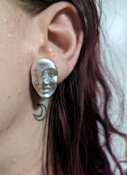 Silver oval face stud earrings on ear, textured metallic finish