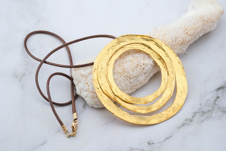 Gold circular pendant necklace with braided cord and textured double-ring pendant